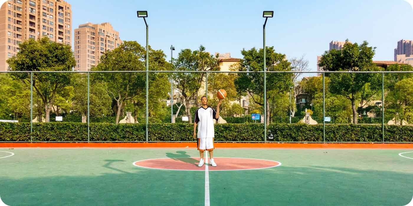 Stojący pośrodku poiska koszykarz z piłką, szeroki widok na niemal całą szerokość boiska Stojący pośrodku poiska koszykarz z piłką, szeroki widok na niemal całą szerokość boiska