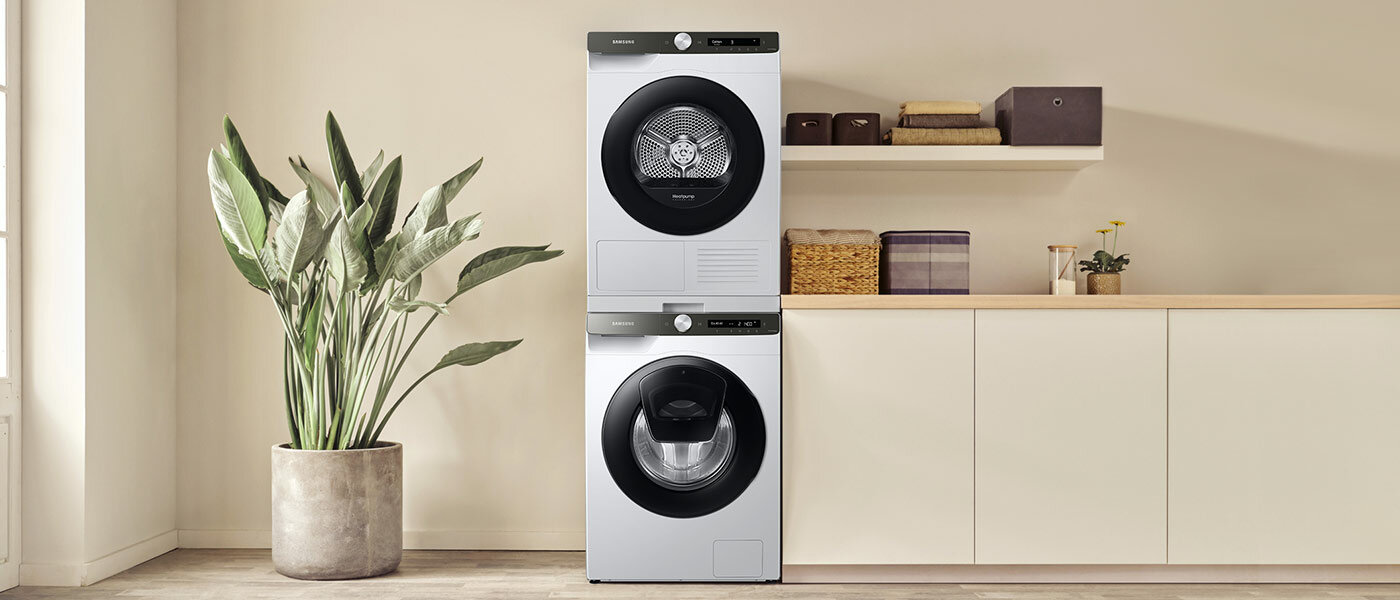 Suszarka a pod nią pralka tej samej serii, obok znajduje się szafa i kwiat Suszarka a pod nią pralka tej samej serii, obok znajduje się szafa i kwiat