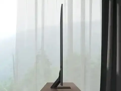 480x360-2025 design neoslim design mo Telewizor o bardzo cienkim profilu stoi na podstawce na tle jasnej zasłony. Widoczny jest tylko bok urządzenia, co podkreśla jego smukłość.